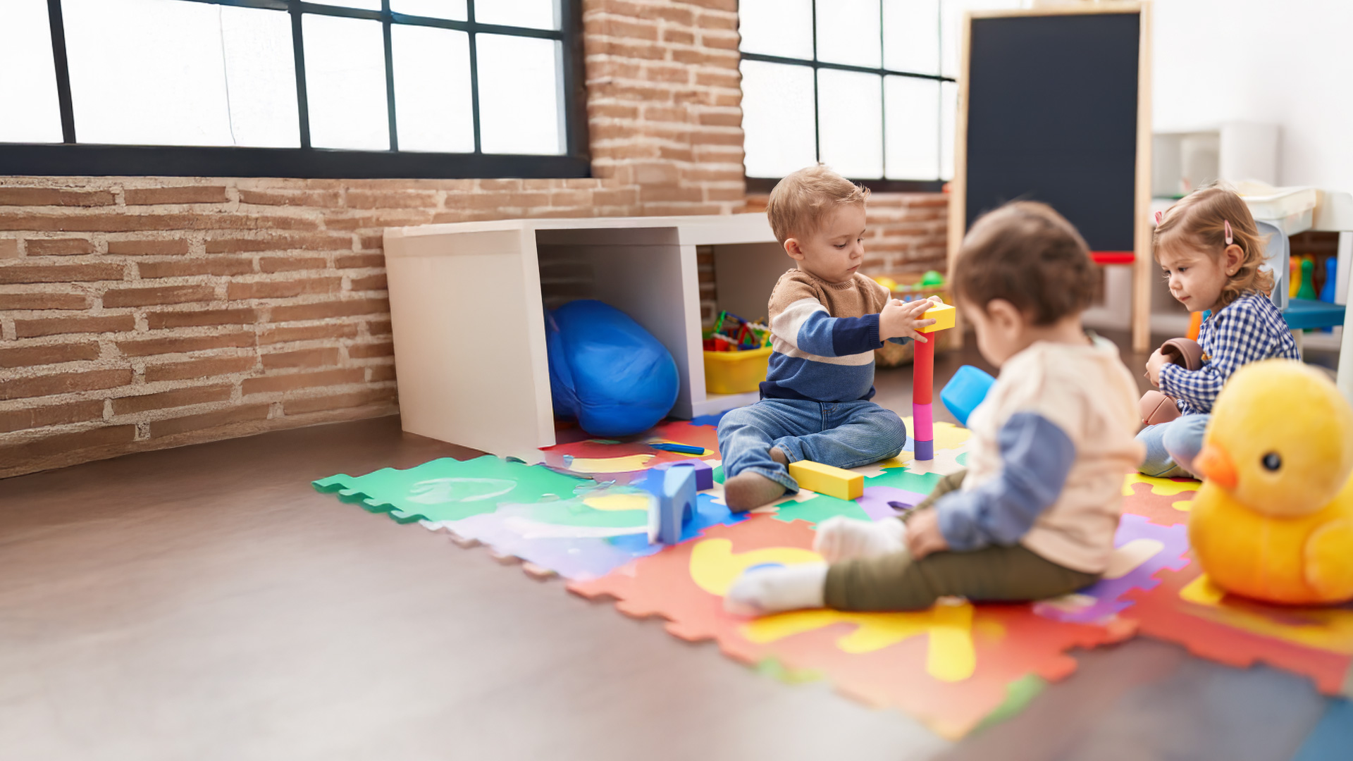 Nursery-aged children sitting on a&nbsp;rug playing with toys.