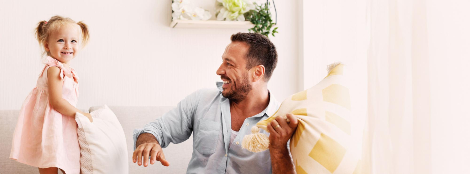 Dad and daughter having a&nbsp;pillow fight, both laughing.