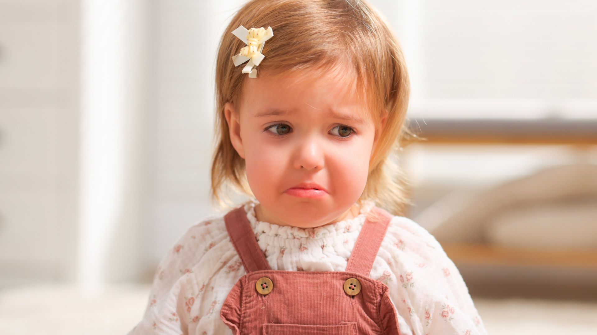 Dziewczynka w&nbsp;wieku 5&nbsp;lat stoi zasmucona, ma blond włosy i&nbsp;jest ubrana w&nbsp;ciuszki w&nbsp;jasnych kolorach.