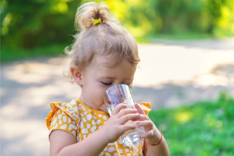 A little girl drinks water straight from a&nbsp;glass.
