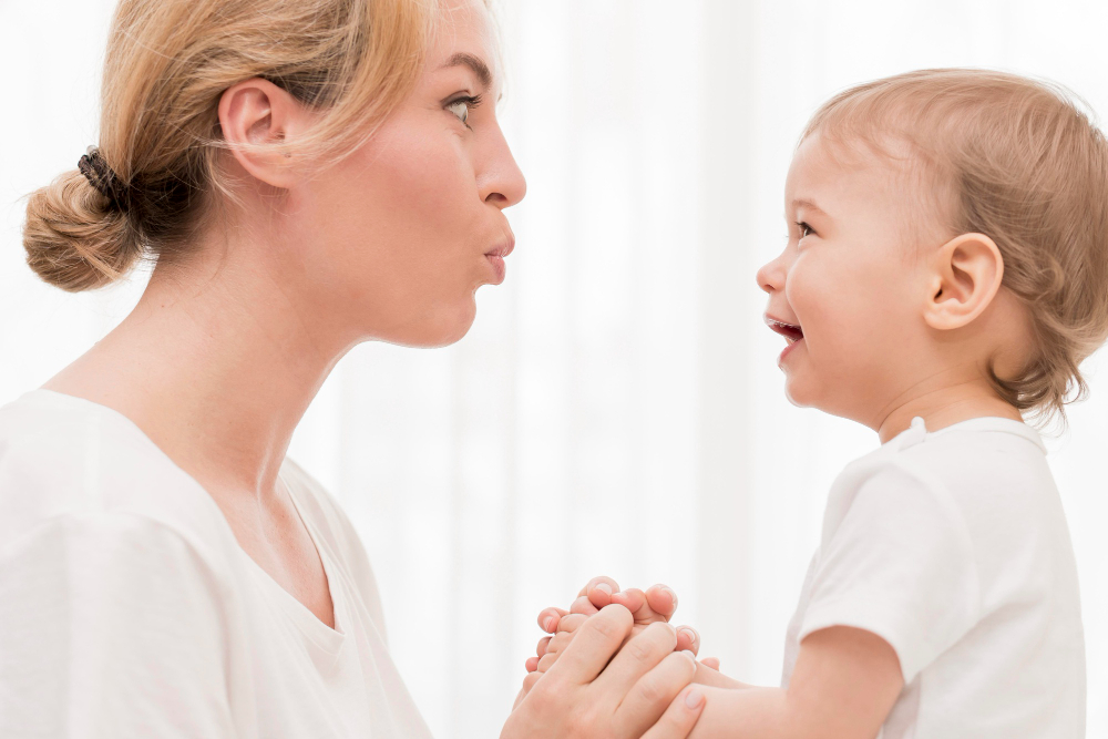 Mama robi śmieszną minę do swojego małego dziecka, oboje są widoczni z&nbsp;profilu.